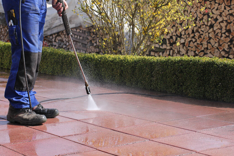 man cleaning brick paver patio with water